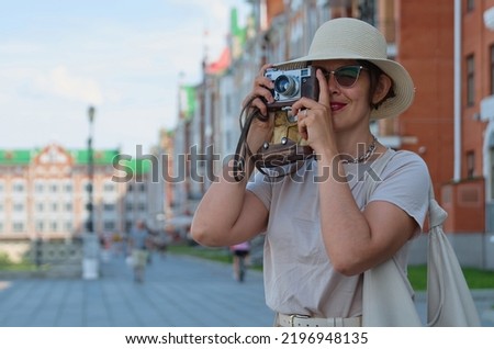 Blue color toned photo of beautiful woman tourist in a straw hat takes pictures on the street with a vintage camera