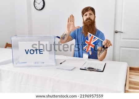 Caucasian man with long beard at political campaign election holding uk flag with open hand doing stop sign with serious and confident expression, defense gesture 