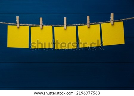 Clothespins with blank notepapers on twine against blue wooden background. Space for text Royalty-Free Stock Photo #2196977563