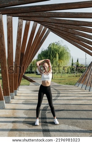 Fit blonde woman wearing black and white sportswear exercising in the park. Close up, copy space, background.