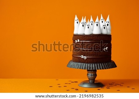 Chocolate Halloween cake with spooky meringue ghosts and candy eyes against an orange background with copyspace to side Royalty-Free Stock Photo #2196982535