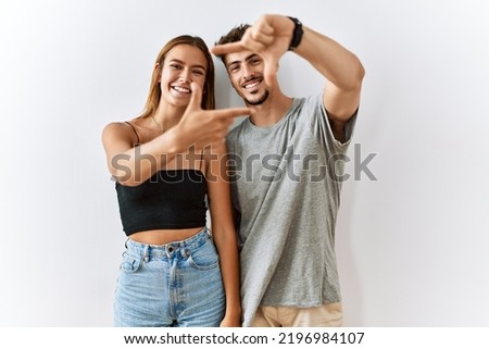 Young beautiful couple standing together over isolated background smiling making frame with hands and fingers with happy face. creativity and photography concept. 