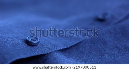 Dark blue shirt button on fabric texture textile material selective focus blurred background. Royalty-Free Stock Photo #2197000511