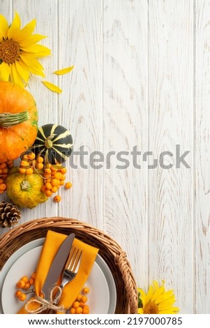 Autumn harvest concept. Top view vertical photo of rattan tray with plate knife fork napkin sunflower pumpkins pattypan pine cone and rowan on isolated white wooden table background with copyspace
