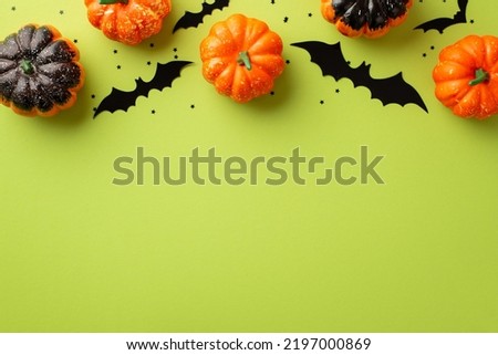 Halloween decorations concept. Top view photo of pumpkins bat silhouettes and black confetti on isolated light green background with copyspace