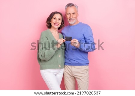 Portrait of two handsome beautiful cheery people holding bank card finance money isolated over pink pastel color background