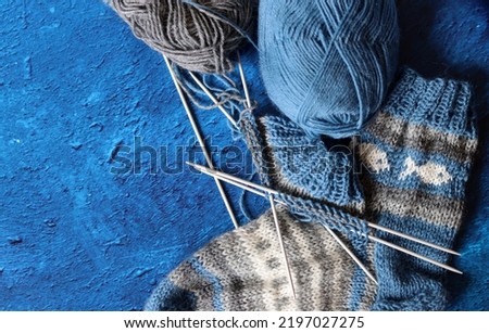 Knitted blue and grey sock, wool balls and needles on textured dark blue background with copy space. Cozy winter concept. 