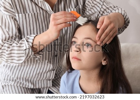 Mother using nit comb on her daughter's hair indoors. Anti lice treatment