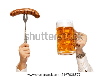 Male hands with grilled sausage on fork and mug with foamy lager beer isolated over white studio background. German and Bavarian holidays. Alcohol, Oktoberfest festival, traditions, taste concept. Royalty-Free Stock Photo #2197038579