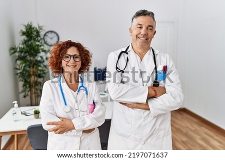 Two middle age doctors at medical clinic happy face smiling with crossed arms looking at the camera. positive person. 