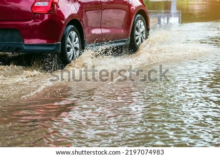 Car passing through a flooded road. Driving car on flooded road during flood caused by torrential rains. Flooded city road with a large puddle. Splash by car through flood water. Selective focus. Royalty-Free Stock Photo #2197074983