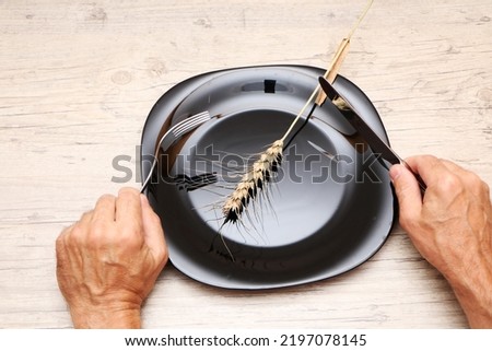 On a black plate, an ear, in the hands of a fork and a knife. A symbol of hunger and inept housekeeping is a plate with cutlery and a spikelet against the background of a wooden structure.