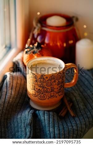 Coffee cup, pumpkins, candle, Halloween decorations on window sill at sunset. Halloween and Thanksgiving home decor.