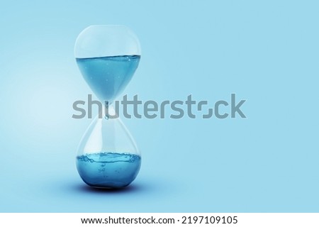 Time as water, a concept. Water with a drip dripping in a glass clock. Creative idea, save the water on a blue background. Global Warming Royalty-Free Stock Photo #2197109105