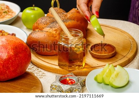 A woman's hand dips an apple in honey at a meal at the festive table in honor of Rosh Hashanah. Horizontal photo Royalty-Free Stock Photo #2197111669