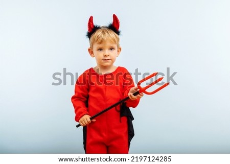 Happy Halloween! Cute little boy in devil halloween costume with horns and trident on light blue background.