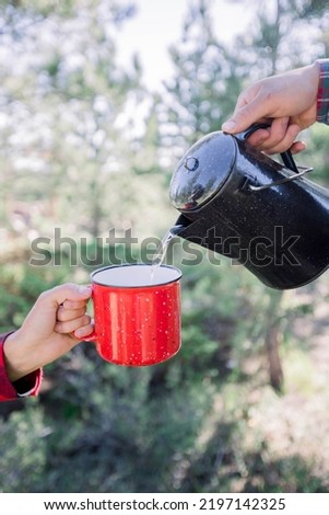 Cropped photo of person pouring hot water from a kettle in to a red cup  