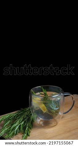 Rosemary herbal tea with lemon slice in a glass cup on wooden table with copy space for your text. Rosemary tea in dark black board surface. Cafe, bar, ethnic, restaurant, hotel concept idea