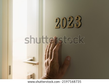 The hand opens the door with the number 2023 behind which light and happiness shine