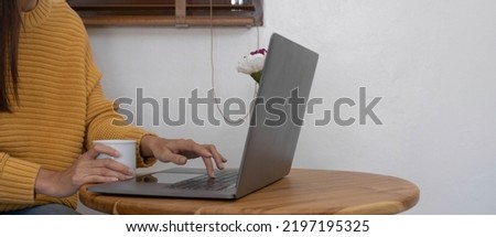 Beautiful young Asian woman holding a cup of hot black coffee on the table while working. Asian young woman enjoy drinking a hot coffee in the morning before starting online meeting from home.
