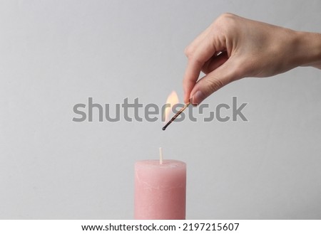 Woman's hand with match sets fire to scented pink wax candle on a gray background Royalty-Free Stock Photo #2197215607