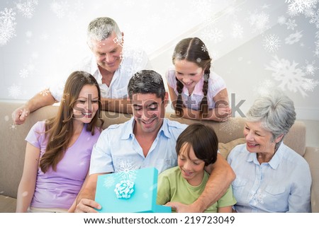 Composite image of Man opening birthday present at home against snowflakes