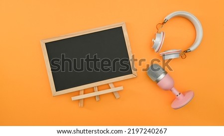Empty black board, wireless headphone and microphone on yellow background. Technology and audio equipment concept