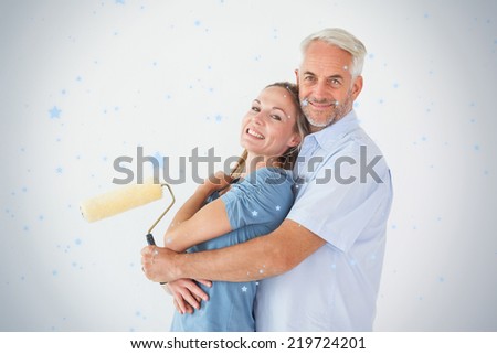 Happy couple hugging and holding paint roller against snow falling
