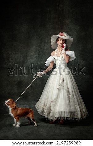 Lady with dog. Vintage portrait of young elegant woman in image of medieval person in renaissance style dress isolated on dark background. Comparison of eras, beauty, history, art, creativity.