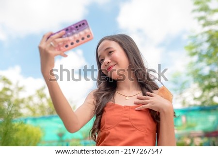 A smiling female teenager takes a selfie using her mobile phone on a hot afternoon.