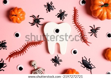 White funny creepy tooth with Halloween decorations on pink background. Dentist Halloween concept. Top view, flat lay.