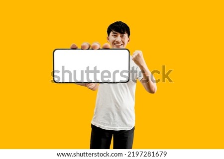 Asian Man Holding Smartphone With Empty White Screen On Yellow Background. Cellphone display Mockup for Mobile App Advertisement.