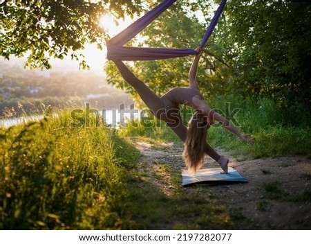 A young gymnast is engaged in aerial yoga in nature in the park, using a combination of traditional yoga poses, pilates and gentle dance