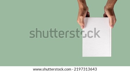 Banner with hand holding closed book mockup on green background in eco style. Template with blank cover about weather, nature, ecology, biology. Space for text. High quality photo