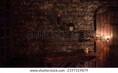 Background of mystical dark interior of medieval room with large wooden door and skull on table against an ancient stone wall. Amazing backgrounds for Halloween holiday. Copy space, text place Royalty-Free Stock Photo #2197319879