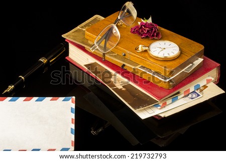 Old book and wood box with old pictures, glasses, dried rose, pen, pocket watch all on a black background with blank space