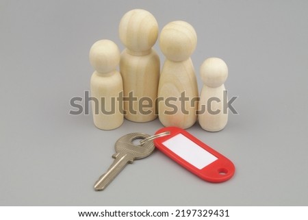 Key with red label and wooden people figures on gray background. Family house concept.