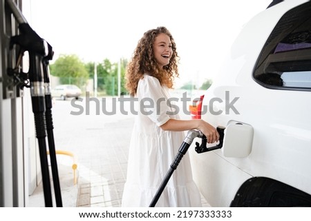 Young curly woman refueling car at gas station Royalty-Free Stock Photo #2197333333
