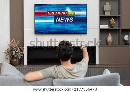 Back view on excited man sitting on the couch and watching breaking news on tv at home Royalty-Free Stock Photo #2197356473