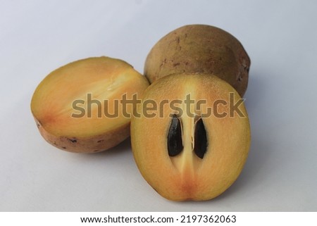 Two sapodillas, one of which is split into two on a white background