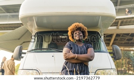 Dark-skinned smiling African young woman with kinky hair in front of her comfortable white camper van. High quality photo