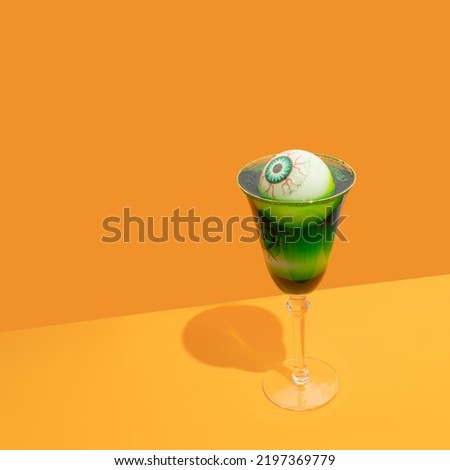 Halloween spooky green cocktail with  bloody eyes on trendy orange background. Festive drink. Halloween party.