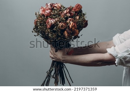 Upset elderly woman hands hold withered dry old rose flowers bouquet Royalty-Free Stock Photo #2197371359