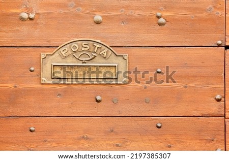 Metal maibox opening on the surface of a wooden exterior front door with the italian word for mail