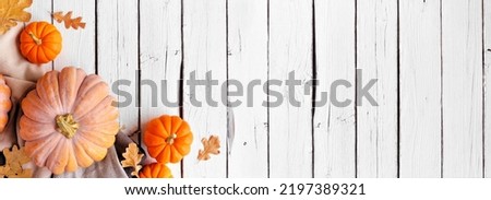 Cozy fall corner border with pumpkins, leaves and blanket. Overhead view on a white wood banner background.