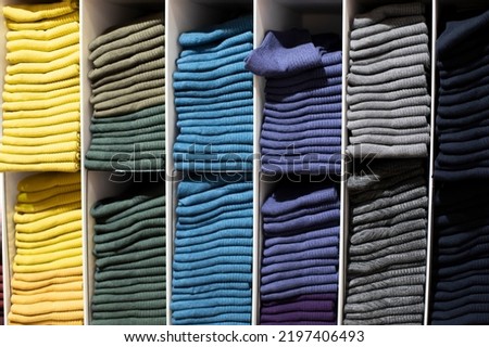 Knitted clothes on a shelf in a store, yellow green gray knitwear. Neat row of clothes in assortment