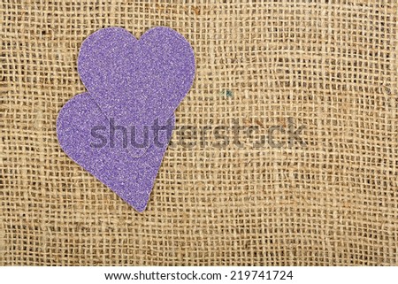 two purple glossy hearts on burlap texture