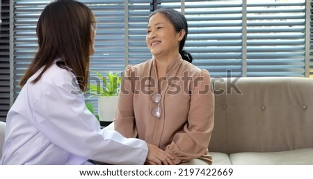 Smiling young female doctor in medical uniform gown enjoying conversation with happy senior woman at home, Mature patient consulting with doctor at home visit sitting together on sofa at home
