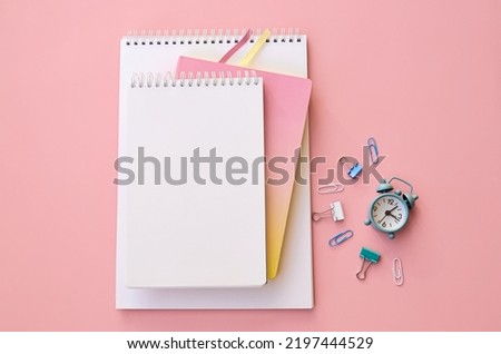 Small alarm clock and notebooks on pink background, flat lay top view. Teaching children education supplies accessories discount sales. Back to school, get ready for learning concept. Copy space.