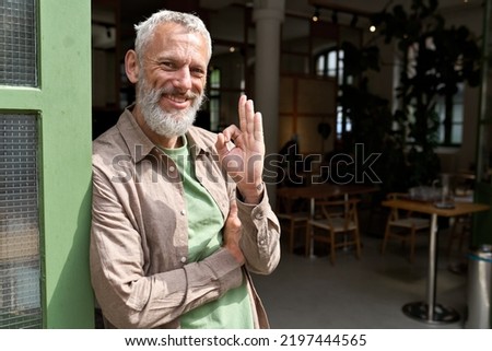 Happy older middle aged man small local business owner showing ok hand sign standing outside cafe or bar giving recommendation or feedback, suggesting good quality welcoming clients. Portrait Royalty-Free Stock Photo #2197444565